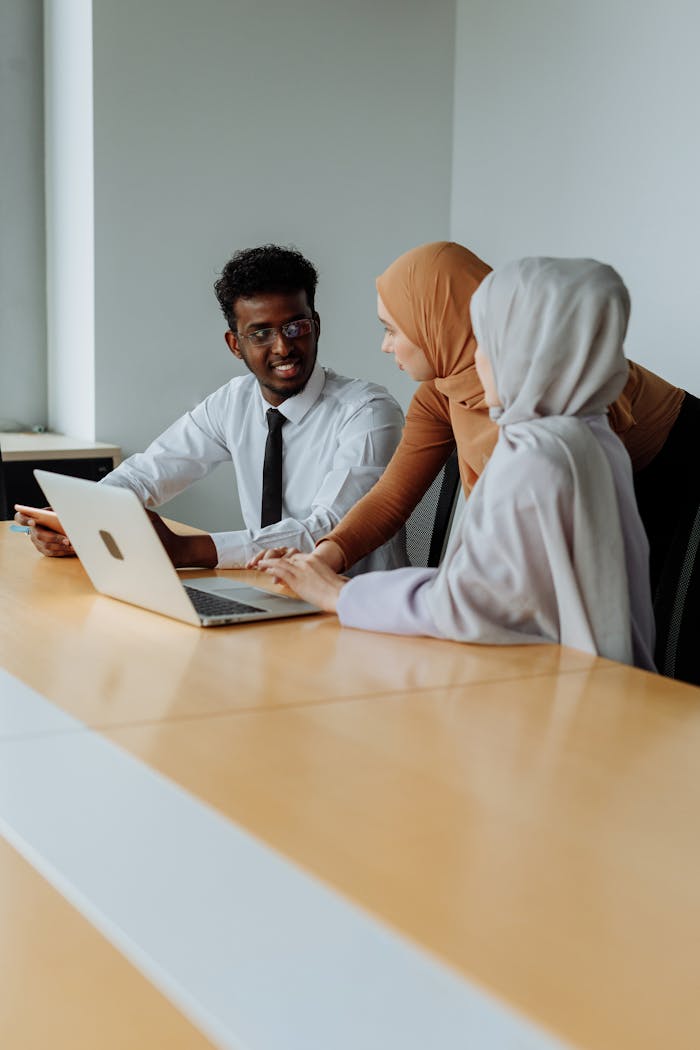 hero-img-02 Three colleagues in an office discussing work, including two women in hijabs and a man with a laptop.